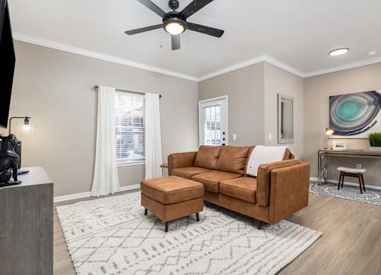 A living room with a brown couch, a television, and a ceiling fan at Clear Creek Meadows Apartments, Copperas Cove, TX, 76522