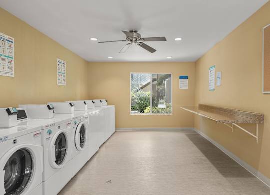 A laundry room with a row of washing machines and a fan on the ceiling.