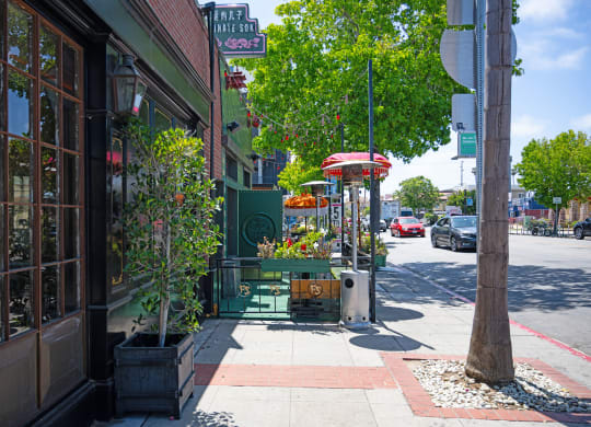a city sidewalk with a green bench and plants on a sidewalk