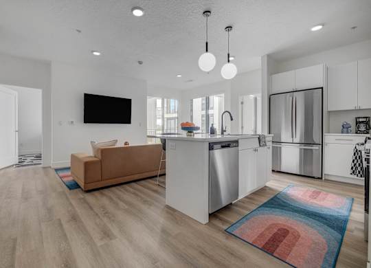 A modern kitchen with a brown sofa and a flat screen TV mounted on the wall.