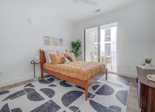 A bedroom with a bed, a rug, and a plant.