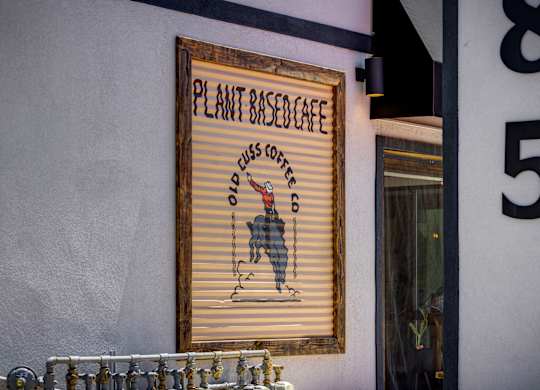 A sign for a plant-based cafe is hanging on a wall.