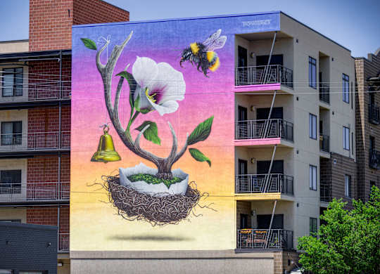 A mural of a flower with a bee and a bell on a building.