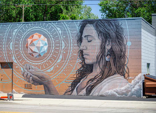 A mural of a woman holding a geometric object is painted on a building.
