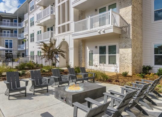 an outdoor patio with chairs and a fire pit in front of an apartment building