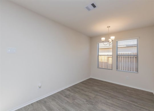 an empty bedroom with two windows and a chandelier at The Village at Granger Pines, Conroe