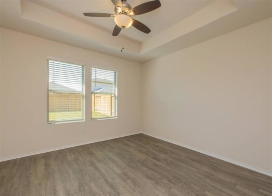 an empty bedroom with a ceiling fan and two windows at The Village at Granger Pines, Conroe, TX 77302