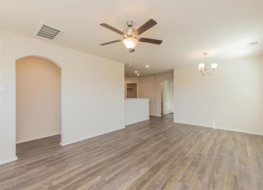 a living room with a ceiling fan and a kitchen in the background at The Village at Granger Pines, Conroe, TX 77302