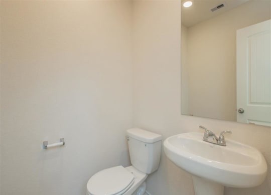 a bathroom with a toilet sink and mirror at The Village at Granger Pines, Texas