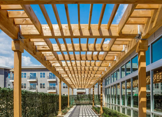 a long walkway under a wooden structure with shadows on the ground