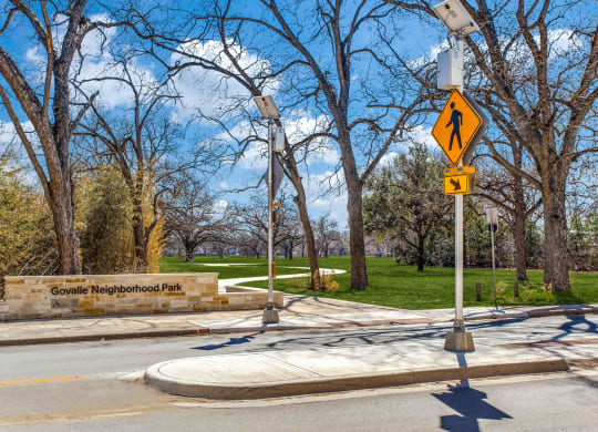a street with a pedestrian crossing sign in front of a park