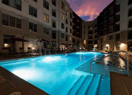 a swimming pool at night in front of an apartment building