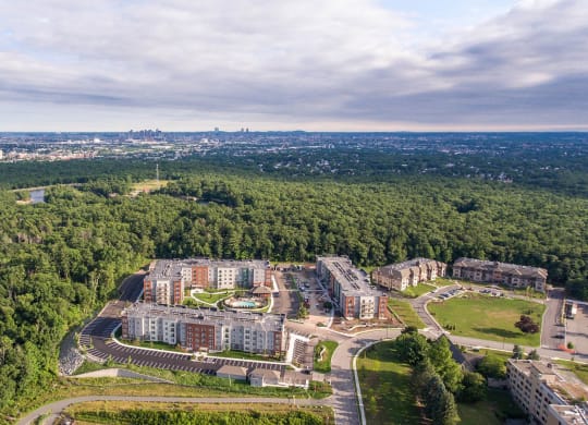 an aerial view of an apartment complex with trees and a city in the background