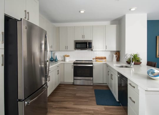Model kitchen at Alta Clara apartments in Stoneham, MA, featuring white countertops and stainless steel appliances.