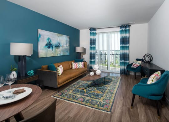 Model living room at Alta Clara apartments in Stoneham, MA, featuring wood grain flooring and a balcony.