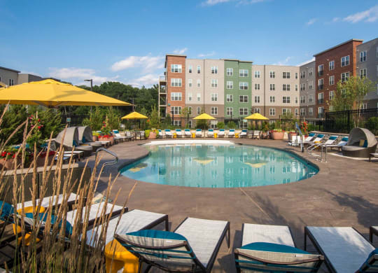 a swimming pool with chairs and umbrellas in front of an apartment building