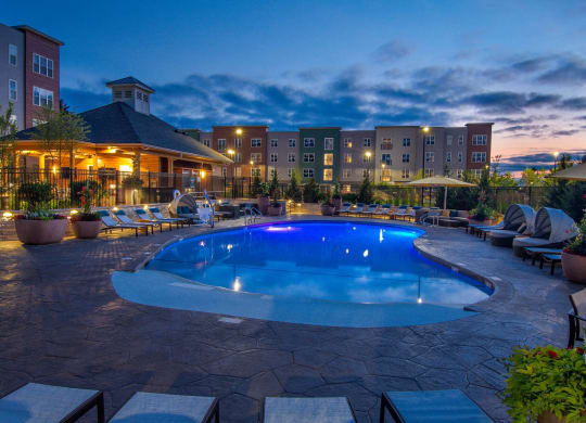 Outdoor swimming pool at Alta Clara apartments in Stoneham, MA, featuring lounge chairs and umbrellas.