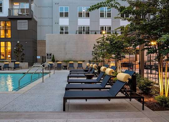 a row of lounge chairs next to a swimming pool in front of an apartment building