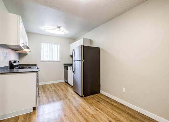 A kitchen with a black refrigerator and wooden floors.