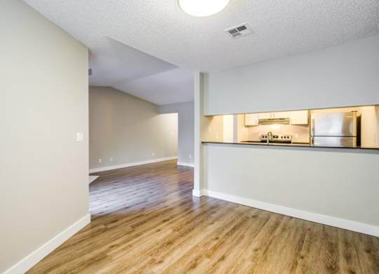 A room with wooden floors and a kitchen area in the background.