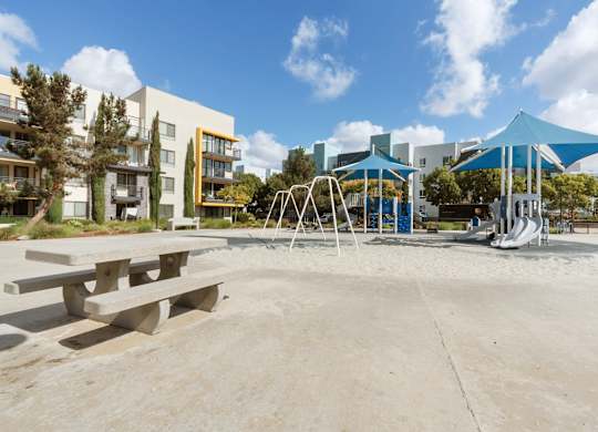 A playground with a blue canopy and a slide is surrounded by buildings.