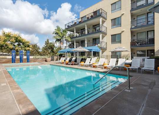 A large swimming pool in front of a building with sun loungers.