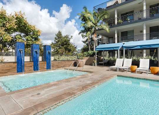 A swimming pool with a blue umbrella and chairs.