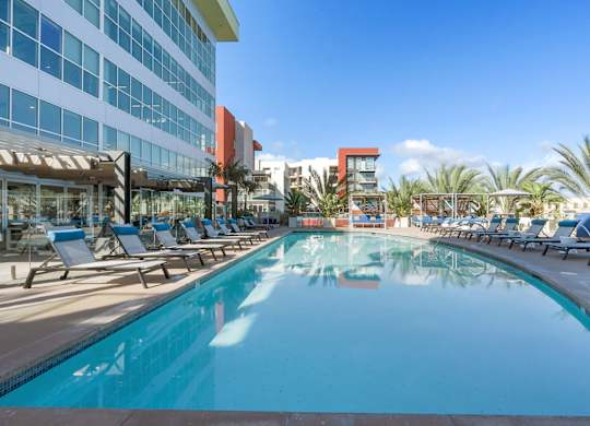 A large swimming pool with lounge chairs and a building in the background.