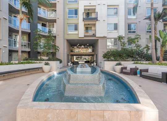 A modern pool with a waterfall in the middle of a courtyard surrounded by buildings.