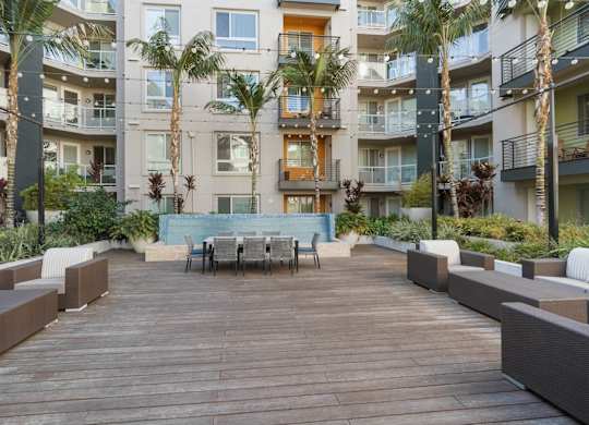 A wooden deck with a table surrounded by palm trees and balconies of apartment buildings.