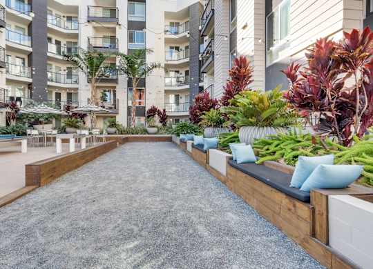A long concrete walkway with a wooden bench on one side and a row of plants on the other.