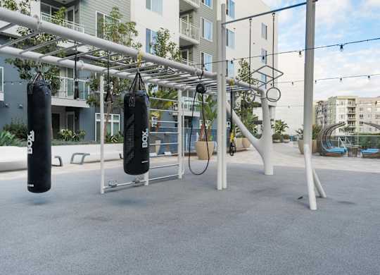 A gym setup with punching bags and rings in front of apartment buildings.