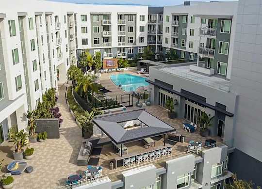 A large outdoor pool area with a table and chairs is surrounded by apartment buildings.