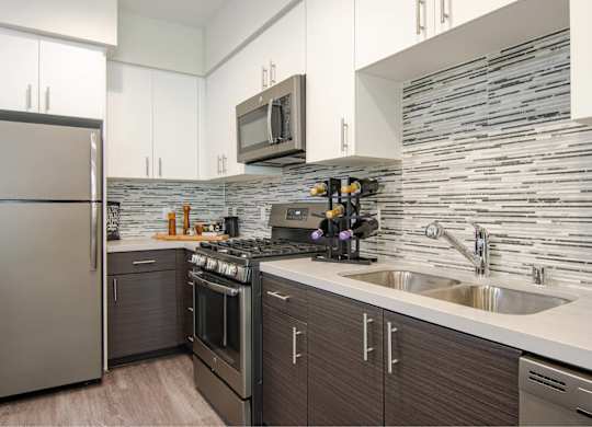 A modern kitchen with a stainless steel refrigerator and a stone backsplash.