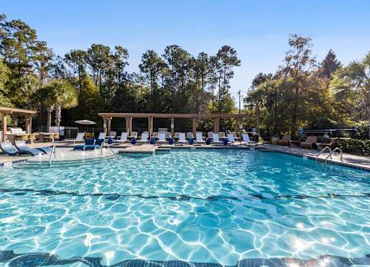 A large swimming pool with sun loungers and a pavilion in the background.