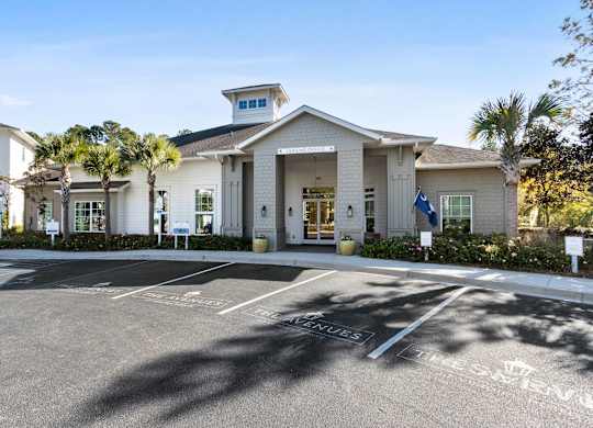 A white building with a flag on the right side and a parking lot in front.