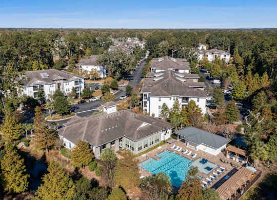 A large white house with a pool in the middle of a wooded area.
