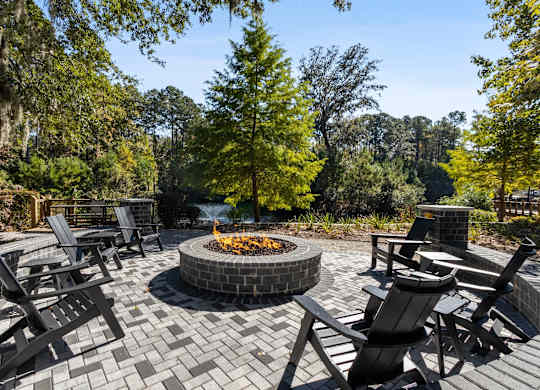 A fire pit in the middle of a brick patio surrounded by chairs.