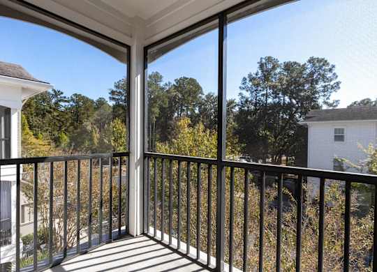 A balcony with a black railing and a view of trees and houses.