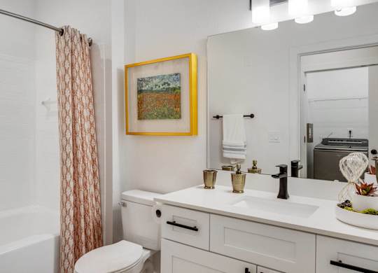 A bathroom with a white toilet, sink, and a painting hanging on the wall.
