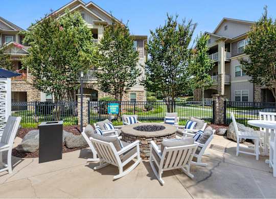 A patio with white chairs and a fire pit in front of apartment buildings.
