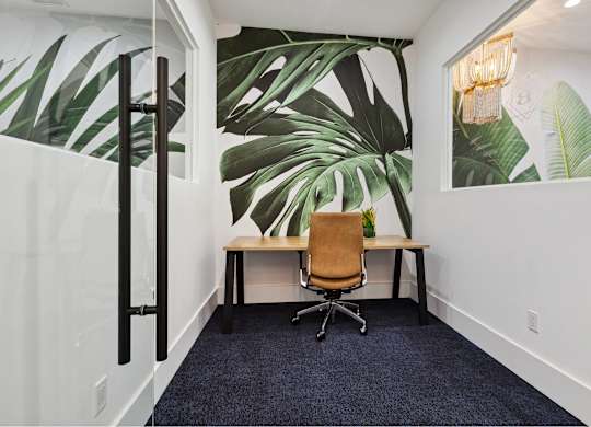 A room with a desk and a chair with a leafy wallpaper.