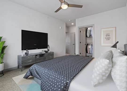A bedroom with a bed, a television, and a ceiling fan.