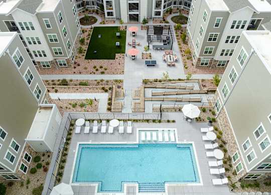 A large swimming pool is surrounded by white lounge chairs and umbrellas.