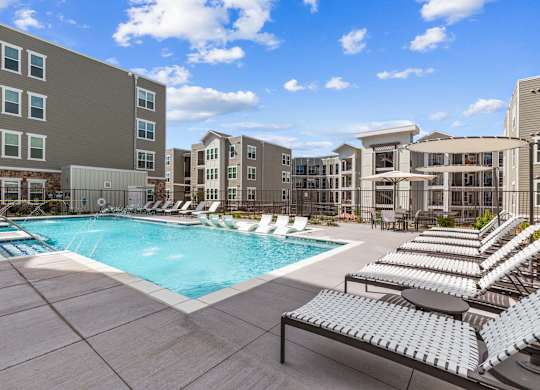 A large swimming pool surrounded by sun loungers and apartment buildings.