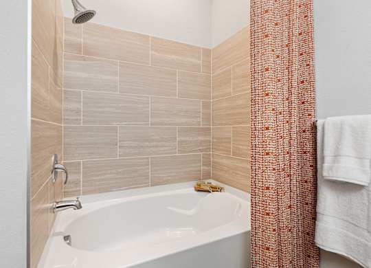 A white bathtub with a shower head and a towel hanging on the wall.