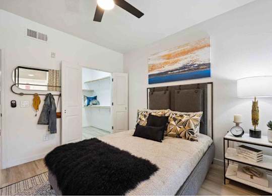 A bedroom with a bed, a ceiling fan, and a painting on the wall.