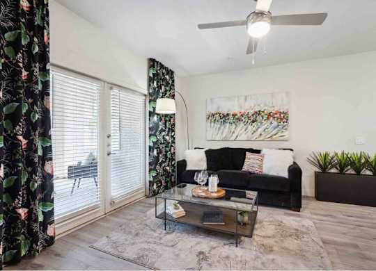 A living room with a black couch, a glass coffee table, and a painting on the wall.
