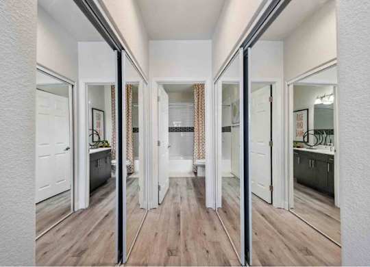 A hallway with white walls and wooden floors, leading to a bathroom with a shower.