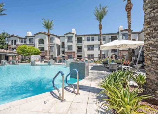 A pool area with a palm tree and a building in the background.